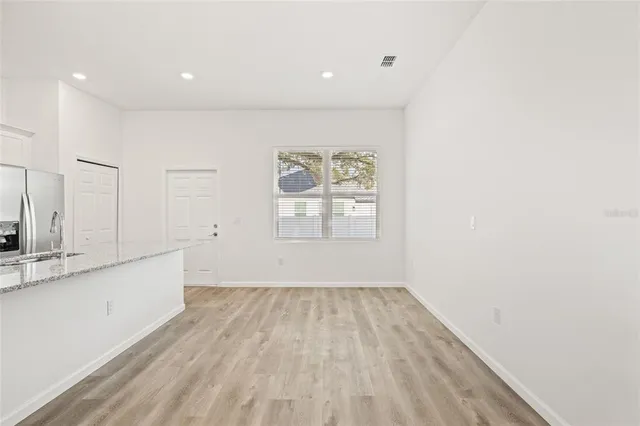 a large kitchen with stainless steel appliances granite countertop a stove a sink a refrigerator and white cabinets with wooden floor