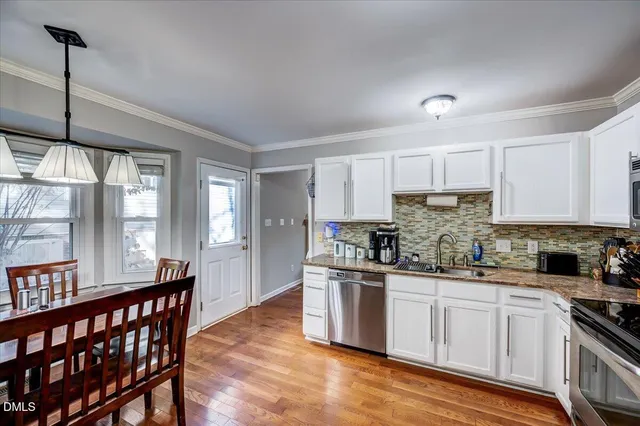 a kitchen with stainless steel appliances a sink a stove a refrigerator cabinets and a dining table with wooden floor