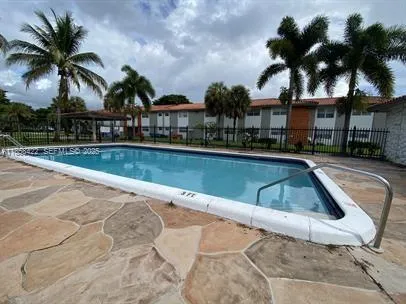 a view of swimming pool that has lawn chairs with plants and palm trees