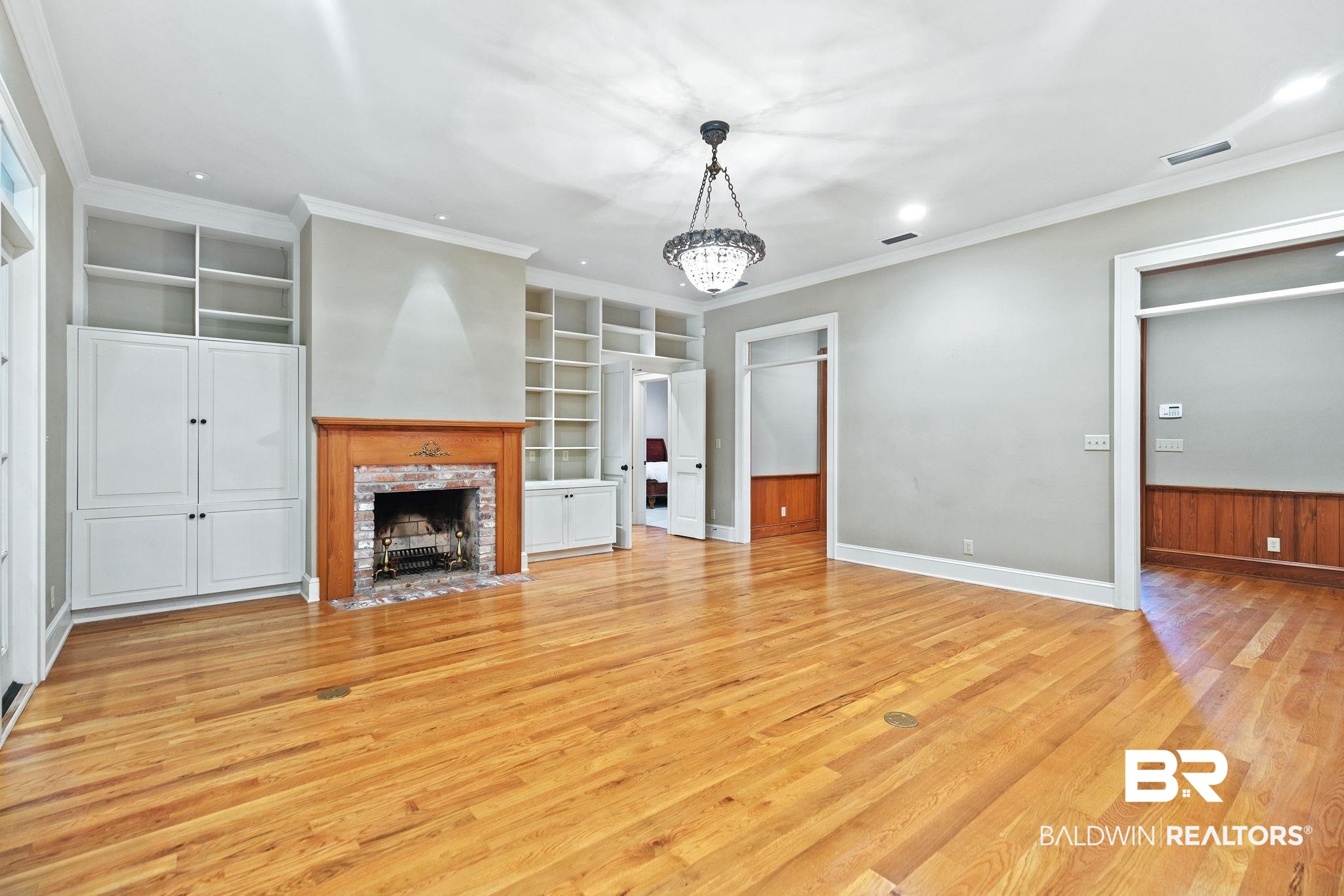 202 Beall Lane Daphne, AL 36526 - Photo 9 of 46 Unfurnished living room with crown molding, light hardwood / wood-style flooring, a chandelier, built in features, and a brick fireplace