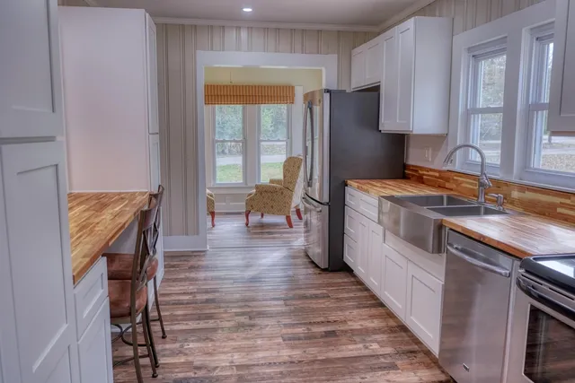 a kitchen with stainless steel appliances granite countertop a refrigerator a sink dishwasher a stove and white countertops with wooden floor