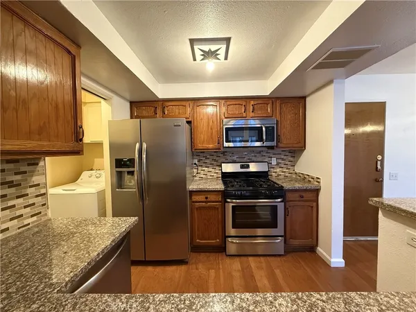 a kitchen with stainless steel appliances granite countertop a refrigerator a stove and a sink with wooden floor