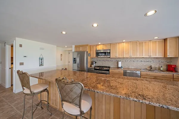 a kitchen with stainless steel appliances granite countertop a stove top oven a sink a dining table and chairs with wooden floor