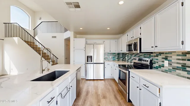 a kitchen with stainless steel appliances a stove top oven a refrigerator a sink and white cabinets with wooden floor