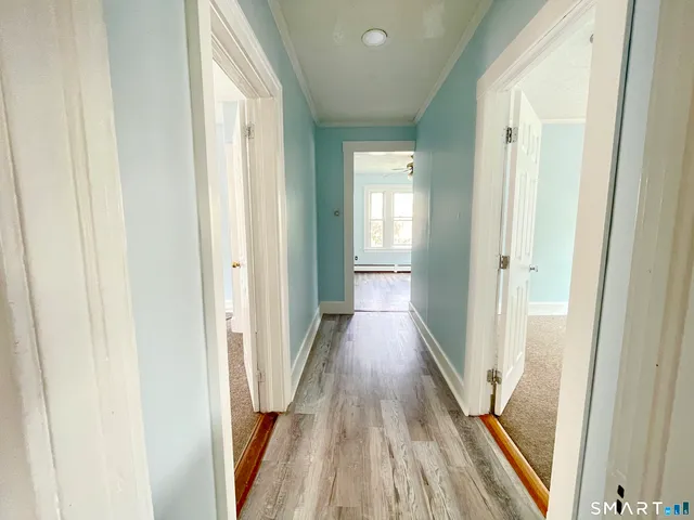 a view of a hallway with wooden floor and a bathroom