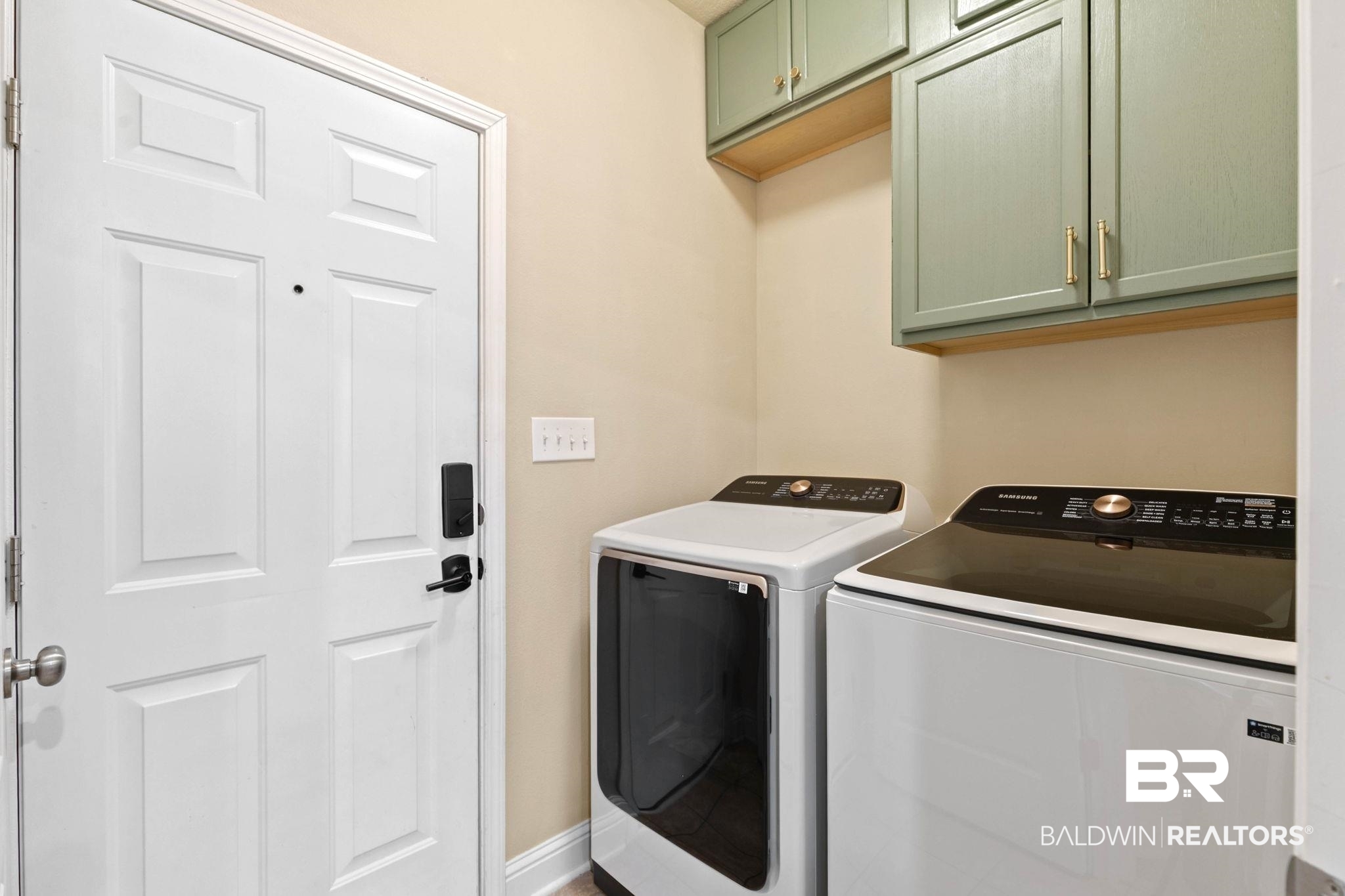 2216 Livingstone Court Mobile, AL 36695 - Photo 37 of 62 Utility space featuring a white paneled door with contemporary black hardware, light-toned walls, green upper cabinetry with gold-toned pulls, and a built-in shelf