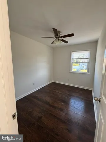 a view of an empty room with wooden floor and a ceiling fan