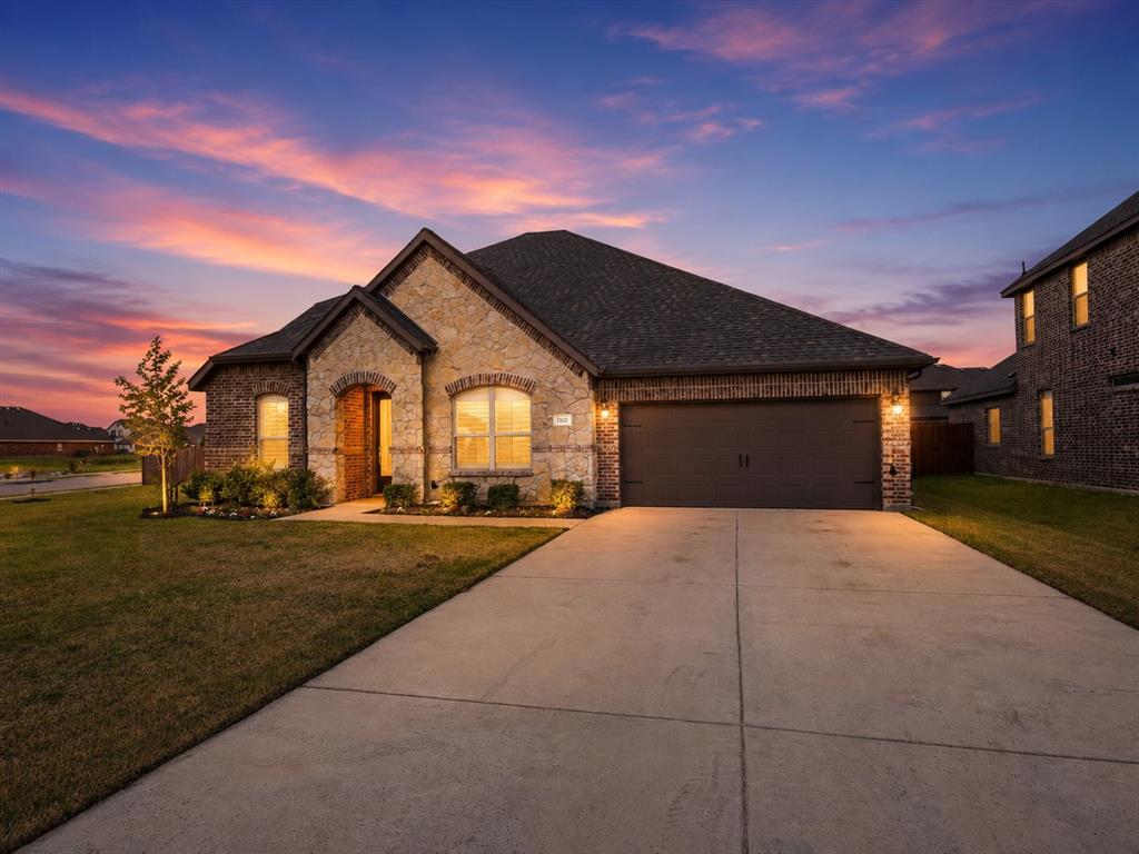 Stone and brick exterior with arched window detailing, dark shingle roof, and an attached two-car garage