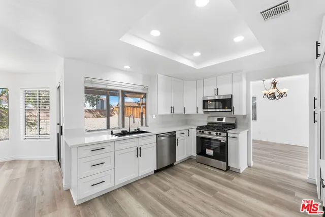 a kitchen with stainless steel appliances granite countertop a stove top oven a sink dishwasher a refrigerator and white cabinets with wooden floor