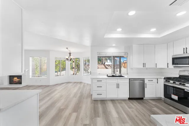 a large kitchen with granite countertop a stove top oven a sink dishwasher and white cabinets with wooden floor