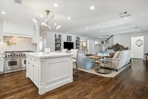 a kitchen with stainless steel appliances kitchen island granite countertop a stove a sink a refrigerator and white cabinets with wooden floor