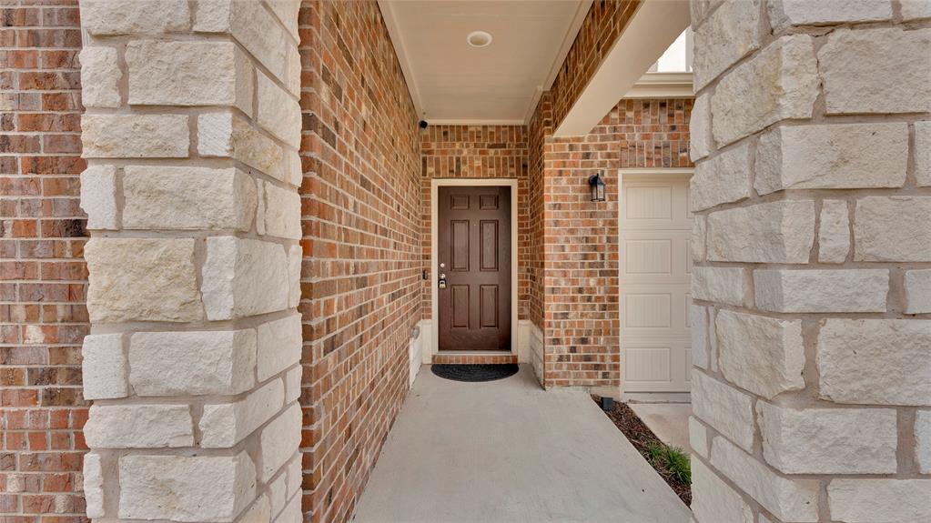 707 Indigo Road Princeton, TX 75407 - Photo 13 of 29 Exterior facade featuring a brown paneled entry door, light brick, stacked stone accents, and a panel-style garage door