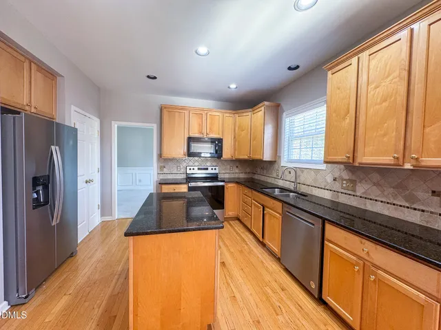 a kitchen with stainless steel appliances granite countertop a refrigerator a sink dishwasher a stove and white countertops with wooden floor