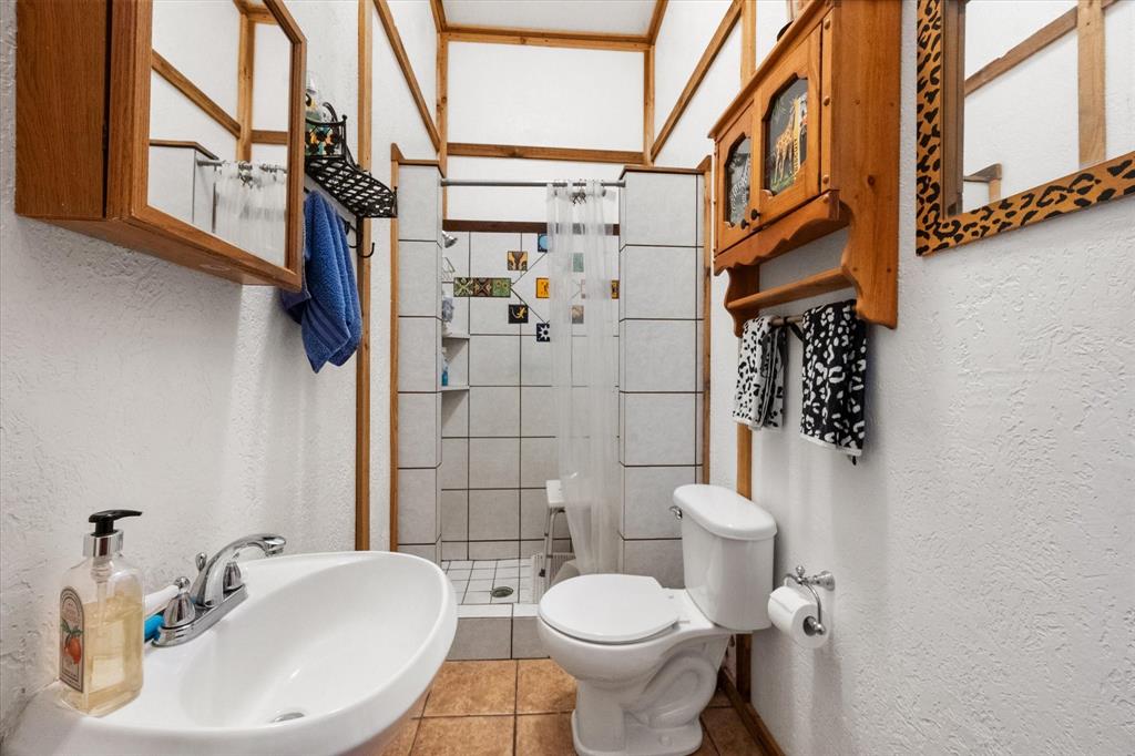 126 Smallwood Court Springtown, TX 76082 - Photo 20 of 24 Secondary Bathroom featuring a tiled shower stall with a clear shower curtain, a ceramic toilet, and a white pedestal sink with a chrome faucet