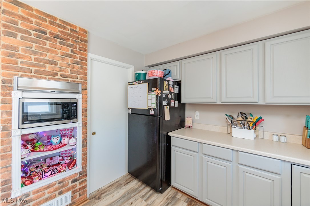 6901 Revere Road Cleveland, OH 44130 - Photo 16 of 50 Kitchen with light hardwood / wood-style floors, white cabinetry, stainless steel microwave, and black fridge