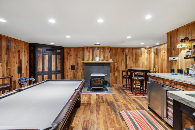 10205 East Moose Loop Road Salt Lake City, UT 84121 - Photo 27 of 50 Reclaimed wood-paneled walls and flooring define this entertainment space, featuring a built-in wet bar with stone countertop, stainless steel beverage refrigerator, and a wood-burning stove with a stone surround