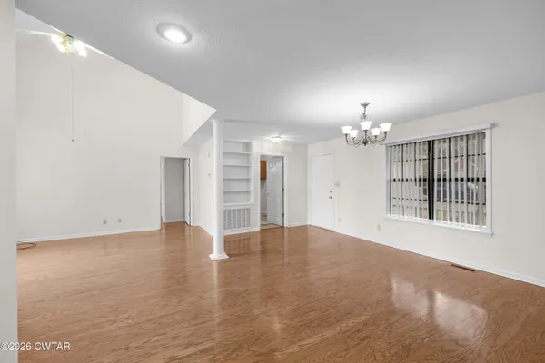 an empty room with chandelier fan and windows