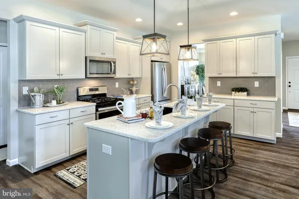a kitchen with stainless steel appliances kitchen island granite countertop a sink a stove a refrigerator and white cabinets with wooden floor