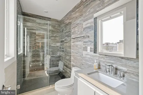 a bathroom with a sink a toilet a glass door a shower and a window