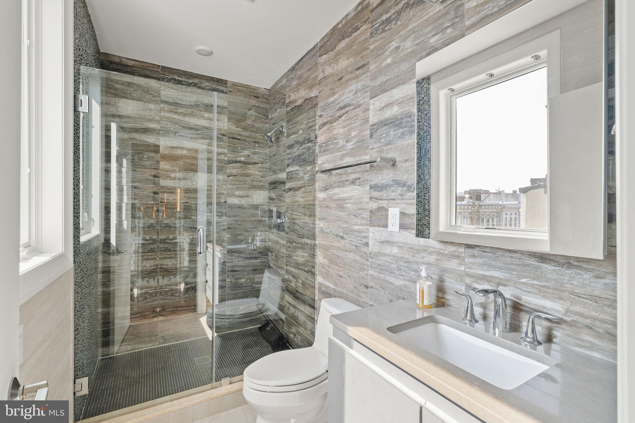 519 Bainbridge Street, Unit A Philadelphia, PA 19147 - Photo 26 of 44 a bathroom with a sink a toilet a glass door a shower and a window