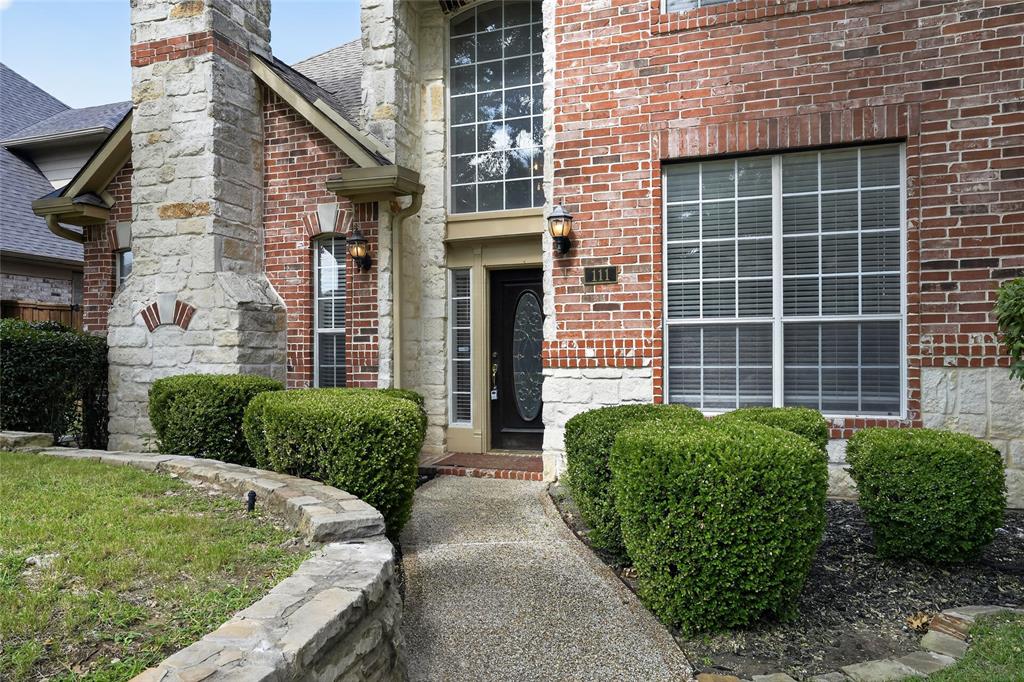 111 Ripplewood Coppell, TX 75019 - Photo 2 of 34 Brick and stone facade featuring a prominent stone chimney, a curved stone retaining wall, and a textured concrete pathway