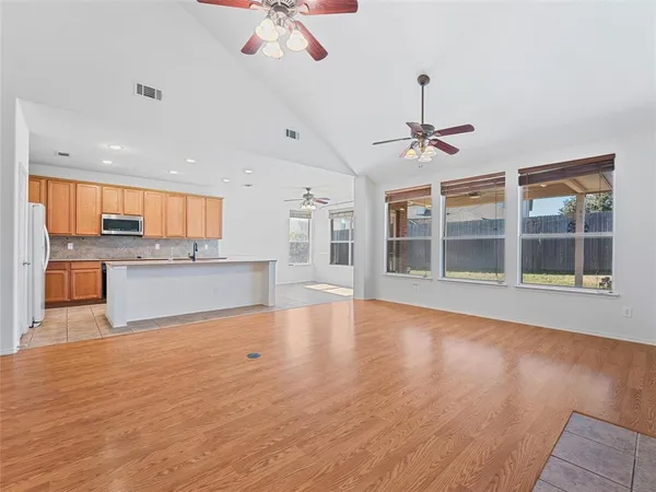 a view of an empty room with wooden floor and a kitchen