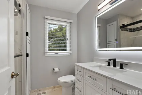 a bathroom with a granite countertop toilet a sink a mirror and a window