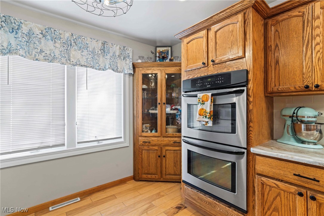 4270 Mellinger Road Canfield, OH 44406 - Photo 11 of 49 Kitchen featuring stainless steel double oven, brown cabinets, granite countertops, light wood-type flooring, and decorative backsplash