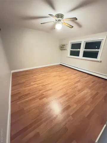 a view of an empty room with wooden floor and a ceiling fan