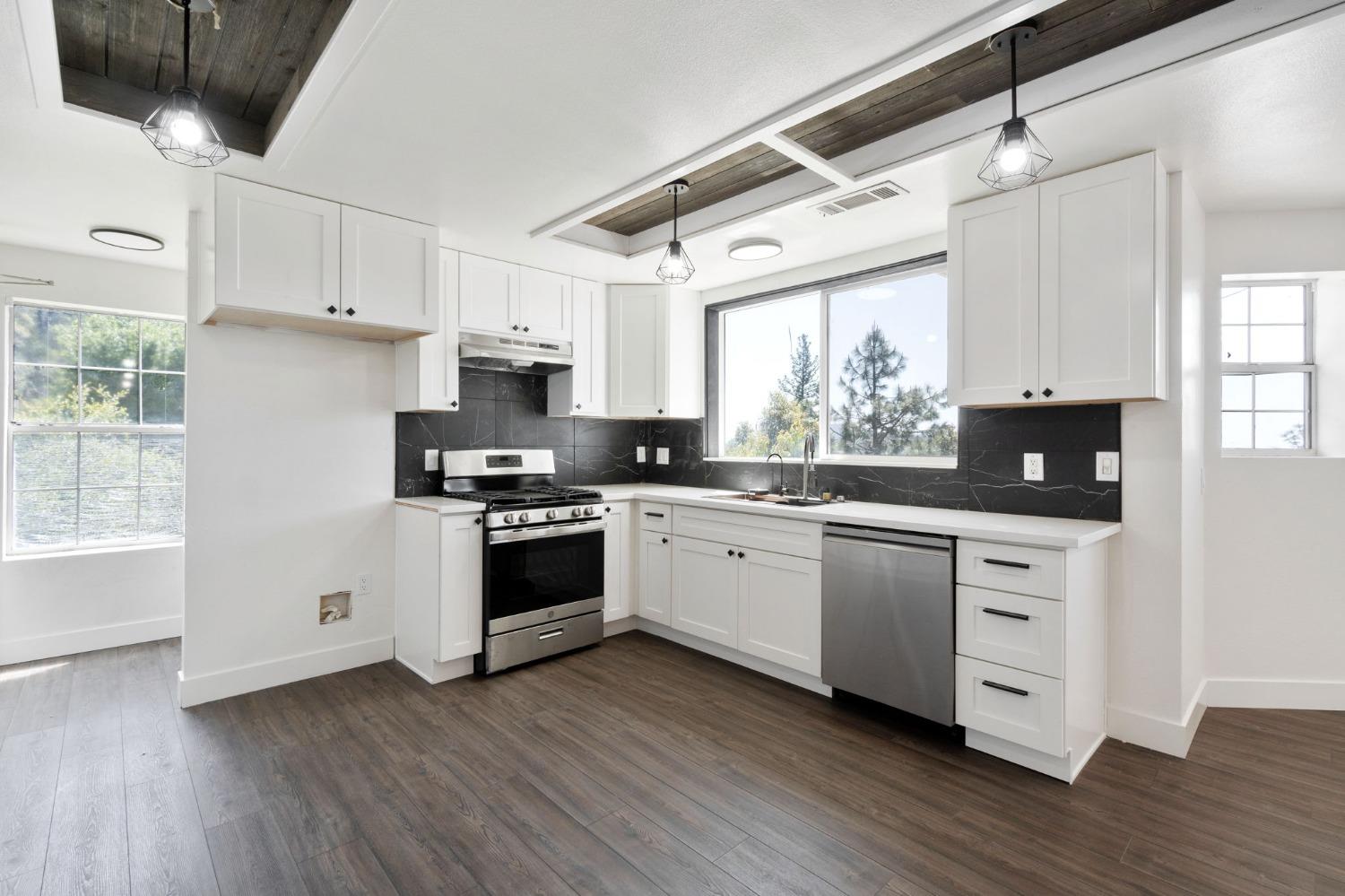 2832 East Westfall Road Mariposa, CA 95338 - Photo 9 of 38 a kitchen with stainless steel appliances white cabinets a sink a stove a microwave and wooden floors