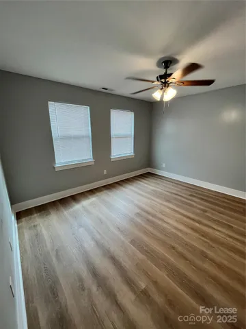 an empty room with wooden floor chandelier fan and windows