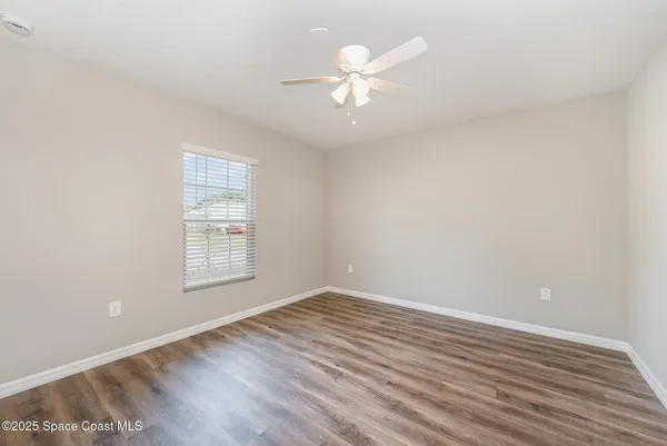 an empty room with wooden floor chandelier fan and windows