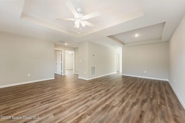 a view of an empty room with wooden floor and a ceiling fan