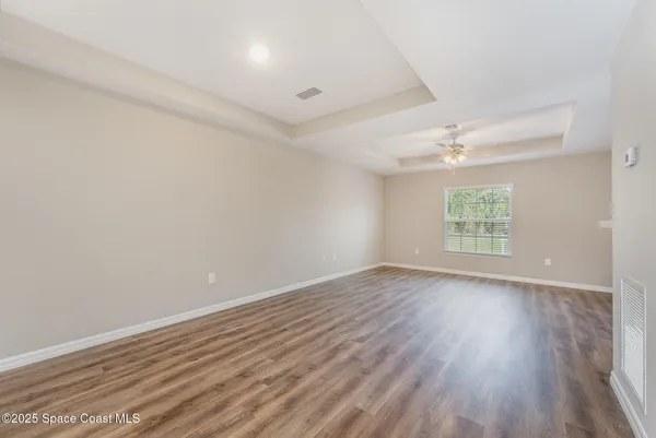 an empty room with wooden floor chandelier fan and windows