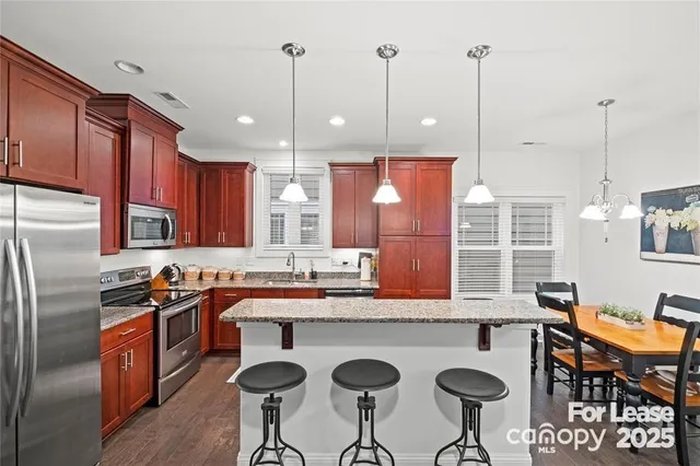 a kitchen with stainless steel appliances granite countertop a sink a stove a refrigerator a kitchen island with chairs and cabinets