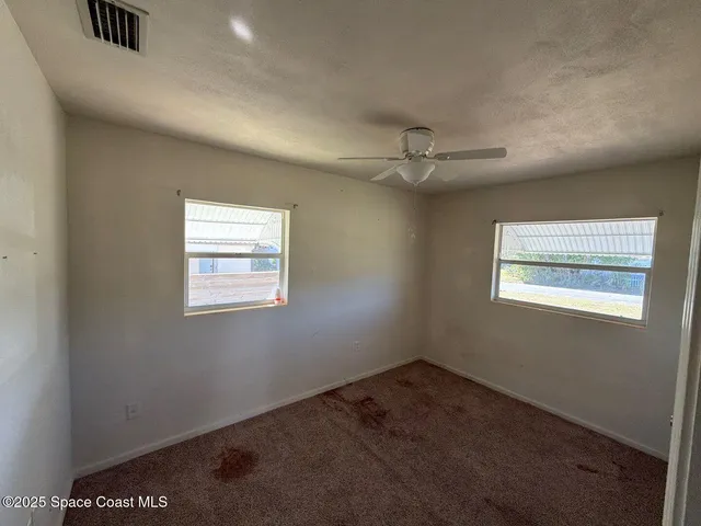 an empty room with a ceiling fan and windows