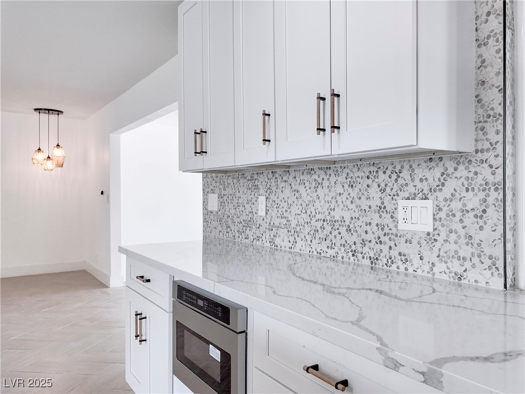 4501 South Woodcrest Road Las Vegas, NV 89121 - Photo 12 of 78 Kitchen with light stone counters, decorative backsplash, white cabinetry, hanging light fixtures, and stainless steel microwave