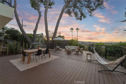 a view of a roof deck with table and chairs couches under an umbrella with wooden floor and fence
