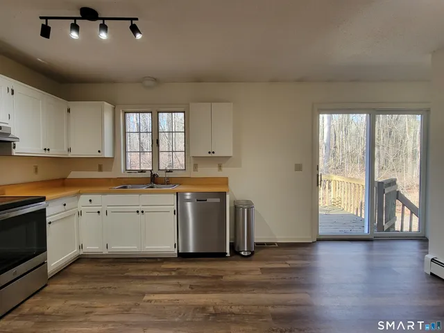 a kitchen with stainless steel appliances granite countertop a stove a sink and white cabinets with wooden floor next to windows