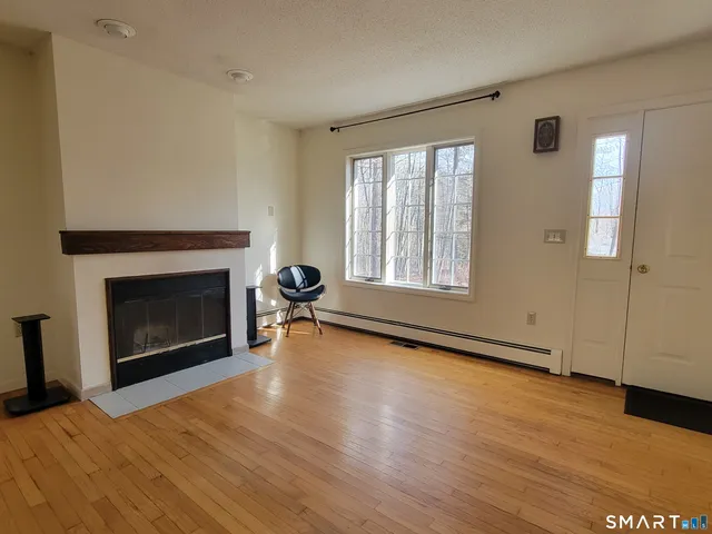 a view of an empty room with wooden floor fireplace and a window