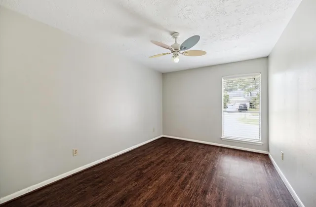 an empty room with wooden floor fan and windows