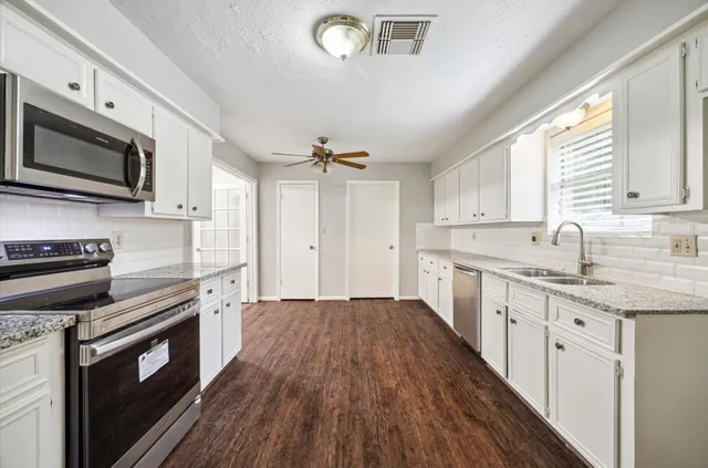 a kitchen with granite countertop a sink wooden floor and stainless steel appliances