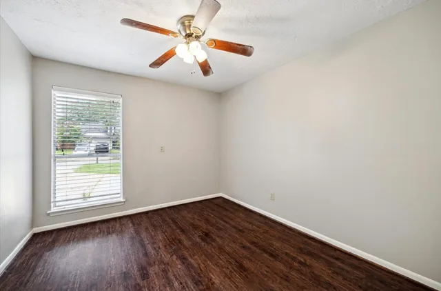 an empty room with wooden floor fan and windows