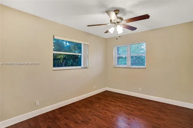 a view of an empty room with wooden floor and a ceiling fan