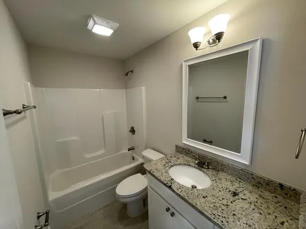 a bathroom with a granite countertop sink toilet mirror and shower