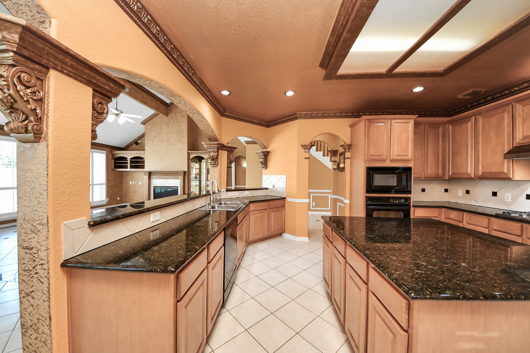 20111 Biscayne Hill Court Spring, TX 77379 - Photo 13 of 44 This spacious kitchen features elegant wooden cabinetry, granite countertops, and decorative arches. It opens to a living area with large windows and a fireplace, offering a warm and inviting atmosphere.