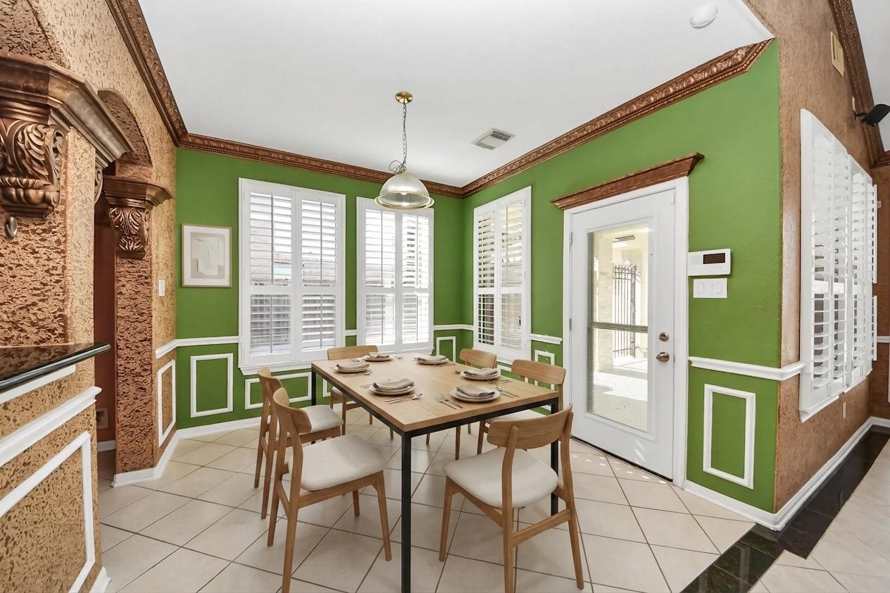 20111 Biscayne Hill Court Spring, TX 77379 - Photo 15 of 44 This dining area features a vibrant color scheme with green and textured brown walls, white trim, and a tiled floor. It includes a wooden dining table with chairs, large windows with shutters for natural light, and a glass door leading outside. The space is accented with ornate molding and a modern light fixture.