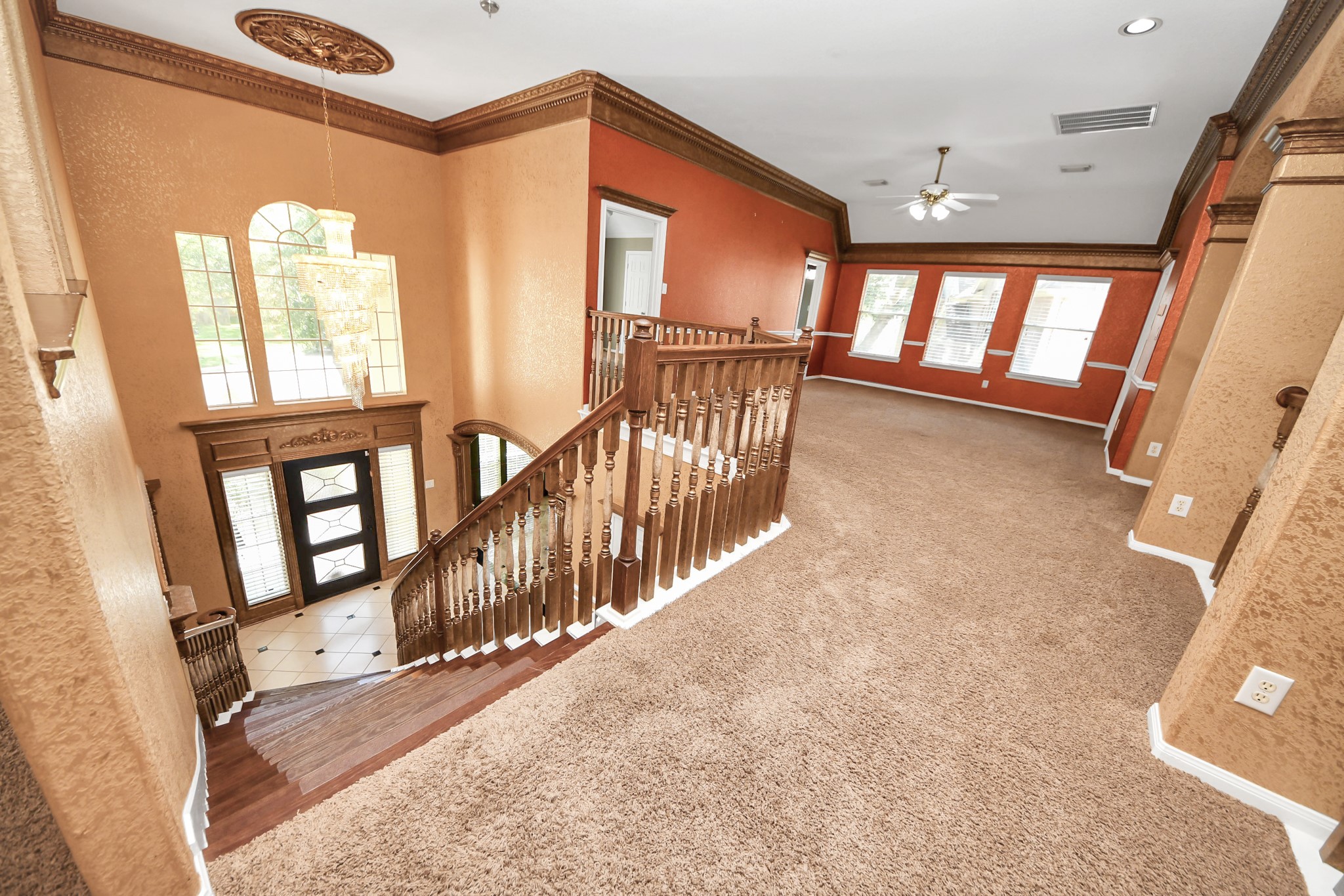 20111 Biscayne Hill Court Spring, TX 77379 - Photo 27 of 44 This photo showcases a spacious, carpeted upper landing area with elegant wood railings and a view of a grand entrance featuring large windows and a chandelier. The space is well-lit with multiple windows, and has warm-toned walls and crown molding for a sophisticated look.