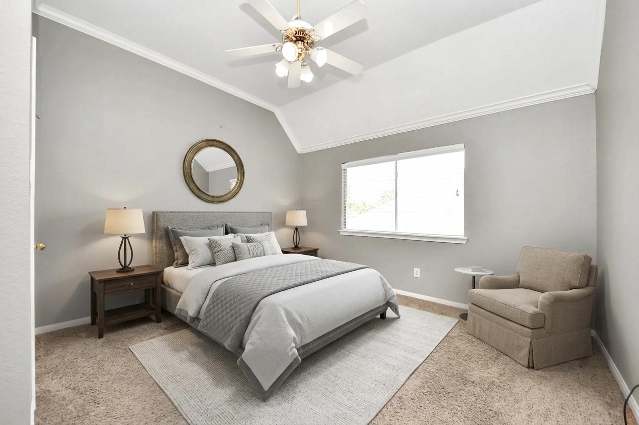 20111 Biscayne Hill Court Spring, TX 77379 - Photo 31 of 44 This bedroom features a cozy atmosphere with neutral tones, a comfortable bed, and a plush carpet. There’s a stylish ceiling fan, ample natural light from the window, and a relaxing armchair. The room is elegantly accented with a round mirror and matching bedside lamps.