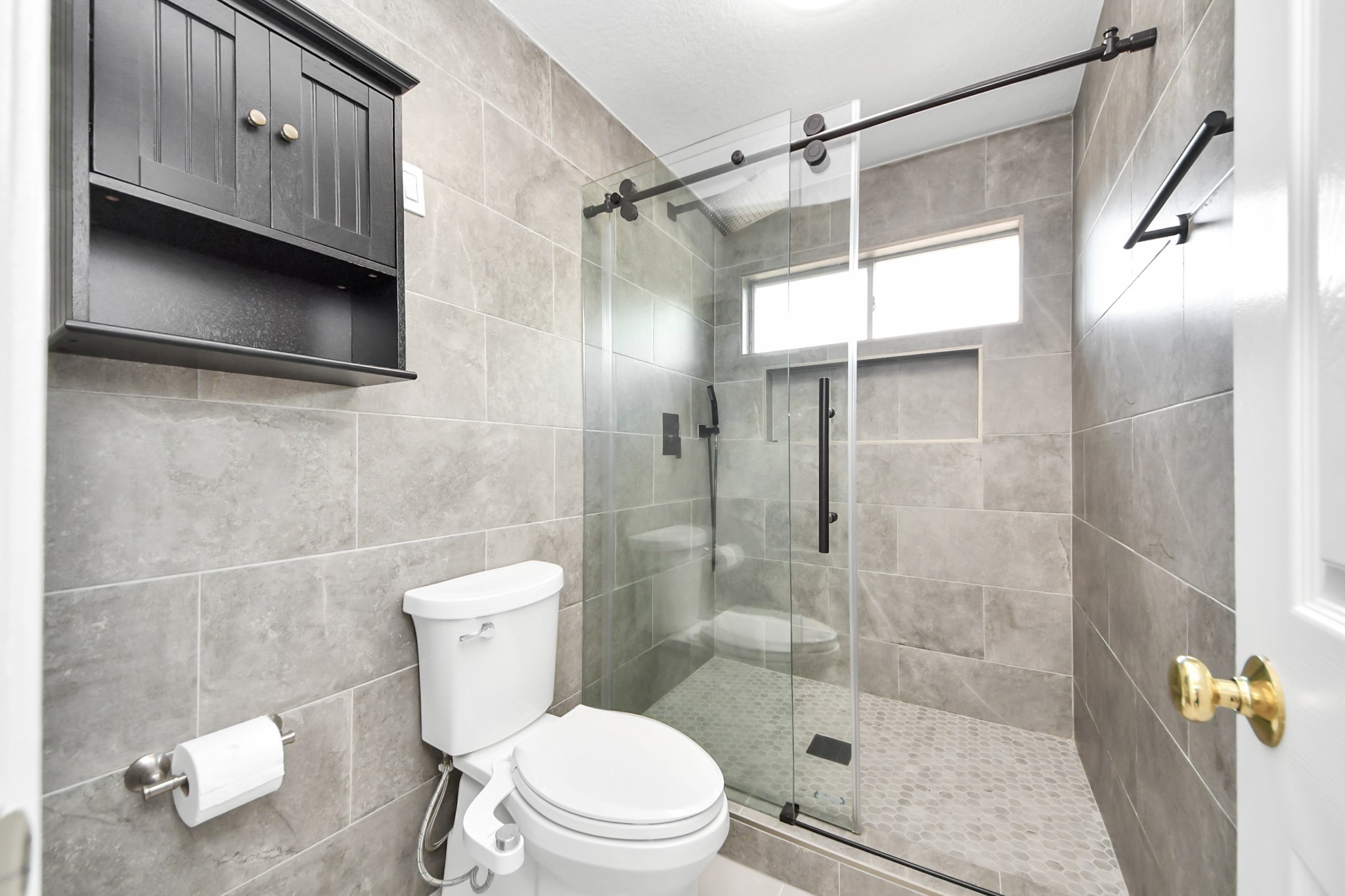 20111 Biscayne Hill Court Spring, TX 77379 - Photo 32 of 44 This bathroom features a modern design with gray tiled walls and floor, a sleek glass-enclosed shower, and a mounted dark wood cabinet for storage.
